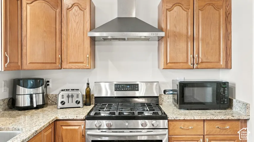 Kitchen featuring raised-panel wood cabinetry, stone-surface countertops, and a stainless steel gas range with a matching wall-mounted ventilation hood