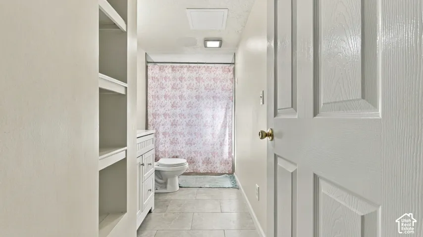 White bathroom vanity featuring shaker-style cabinetry, recessed shelving unit, porcelain tile flooring, and a solid-core six-panel door
