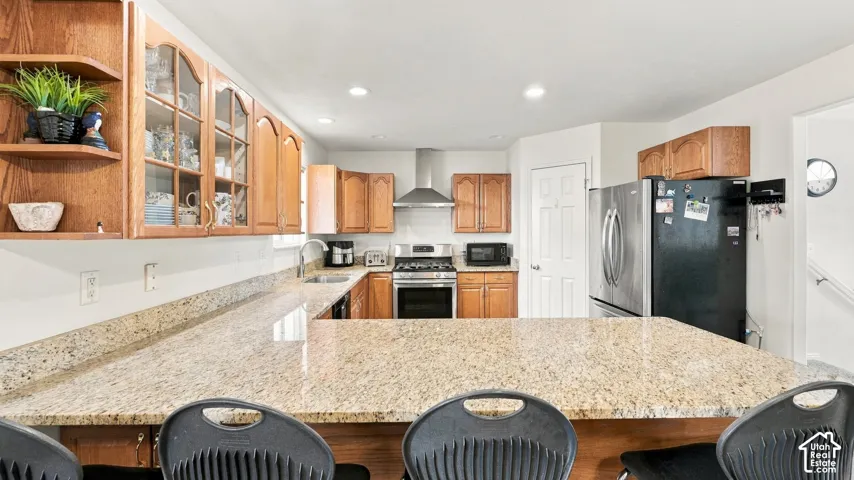 Kitchen featuring natural wood cabinetry, stone countertops with integrated breakfast bar, stainless steel gas range, and recessed ceiling lighting