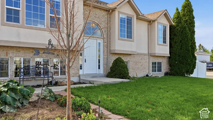 Multi-level exterior featuring a brick and stucco facade, arched entryway, bay windows, and a landscaped front yard
