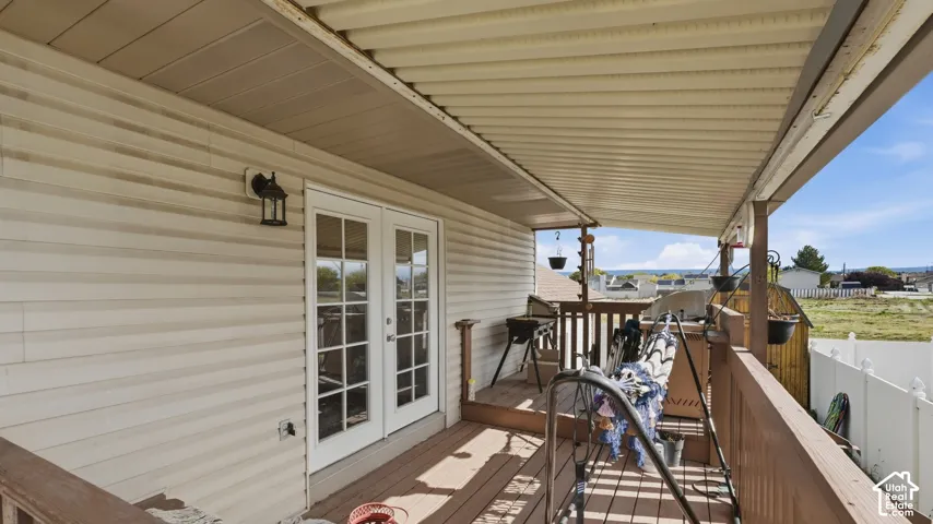 Covered deck featuring vinyl siding, multi-pane French doors, attached wall-mounted lantern lighting, and wood-finish decking with railings