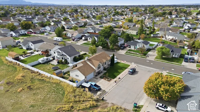Aerial view featuring a two-story residence with an attached garage, a concrete driveway, and a white perimeter fence enclosing a rear yard