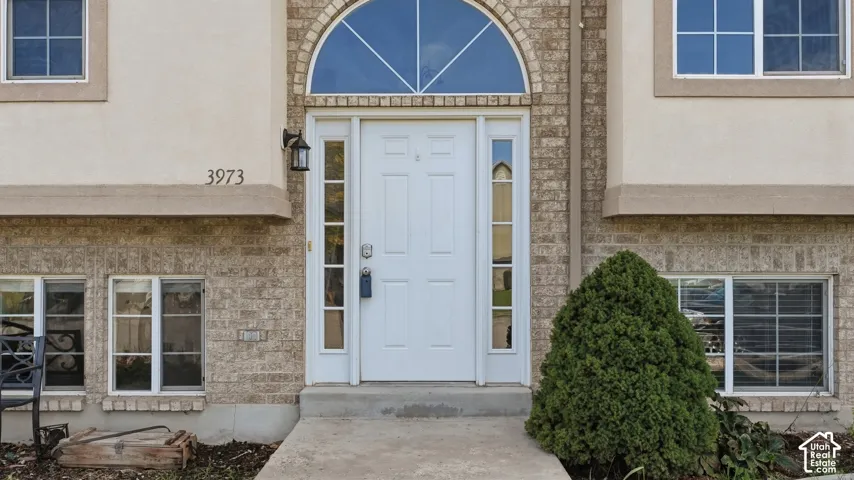 Exterior entryway featuring a brick facade, arched transom window, paneled front door with flanking sidelights, and exterior wall-mounted lighting