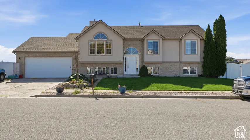 Split-level exterior featuring a brick and stucco facade, an attached two-car garage, arched window detailing, and a concrete driveway