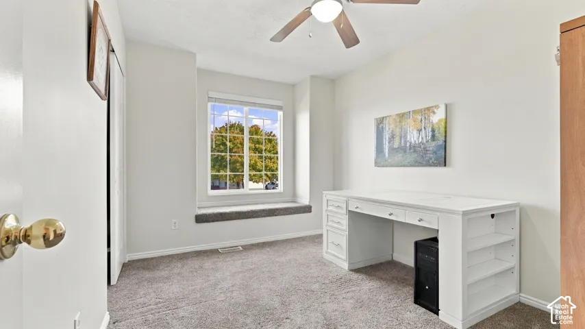 Neutral-toned interior featuring a recessed window seat, multi-pane window, ceiling fan with light fixture, and carpeting