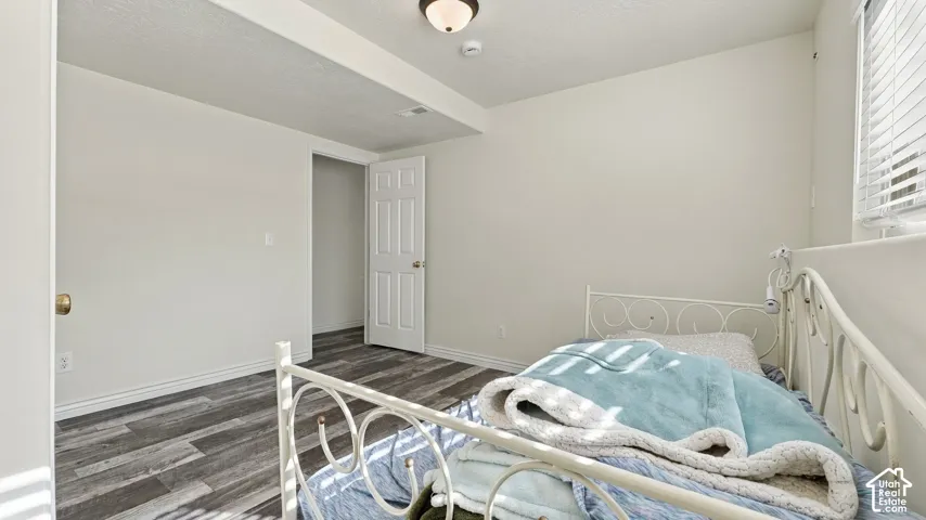 Neutral-toned room featuring wood-finish flooring, a multi-panel interior door, and a horizontal window with adjustable blinds