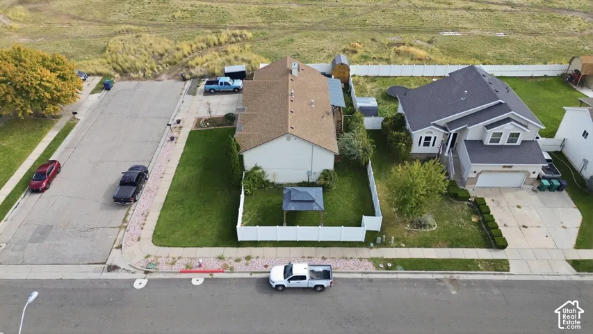 Aerial view of a residential corner lot featuring a fenced backyard, green lawn, concrete driveway, and attached garage