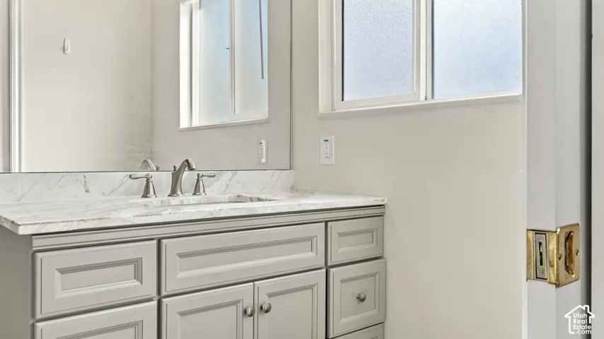 Grey shaker-style vanity featuring a stone countertop with veining, integrated basin, brushed nickel faucet, and a large wall-mounted mirror