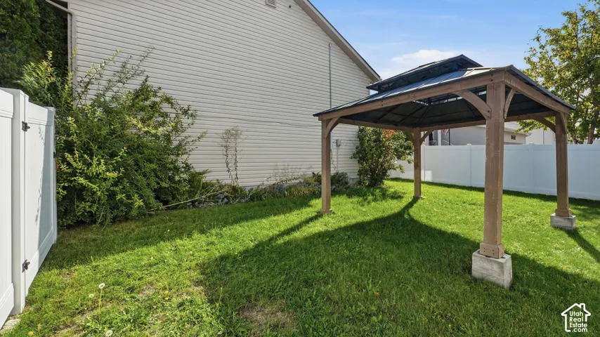 Outdoor space featuring a permanent wooden gazebo with a dark metal roof, vinyl privacy fencing, and a manicured lawn
