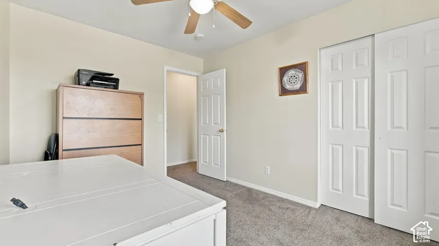 Neutral-toned interior featuring carpeted flooring, a six-panel door, a sliding closet with paneled doors, and a ceiling fan with integrated light fixture