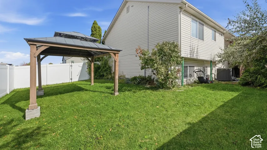 Backyard featuring a wood-frame gazebo with a metal roof, white vinyl privacy fencing, and a manicured lawn