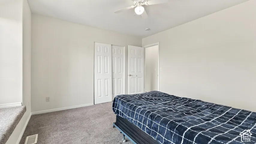 Neutral-toned interior space featuring carpeted flooring, built-in dual-panel closet doors, and a ceiling-mounted light fixture with integrated fan