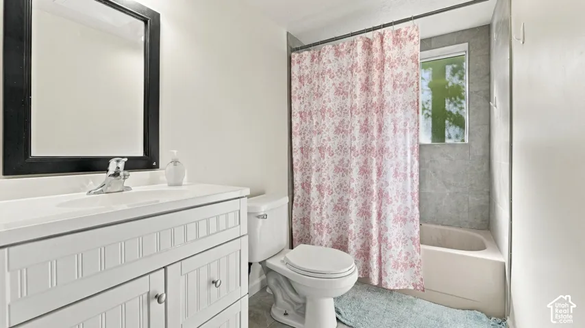 Bathroom featuring a white vanity with beadboard detailing, chrome faucet, framed mirror, and a tub-shower combination with light-toned stone-finish tile surround