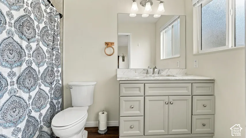 Shaker-style vanity with neutral cabinetry, stone-surface countertop, rectangular undermount sink, three-light fixture, and large wall-mounted mirror