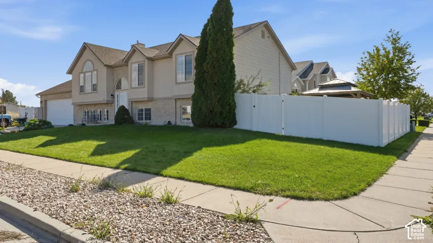 Multi-level exterior featuring vinyl siding, stone-veneer accents, an attached two-car garage, and a fenced backyard with an enclosed pavilion