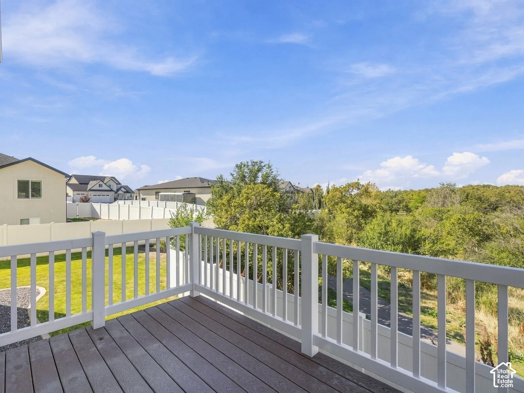 Raised deck featuring synthetic wood-finish decking and white composite railing, overlooking a fenced backyard and mature tree line