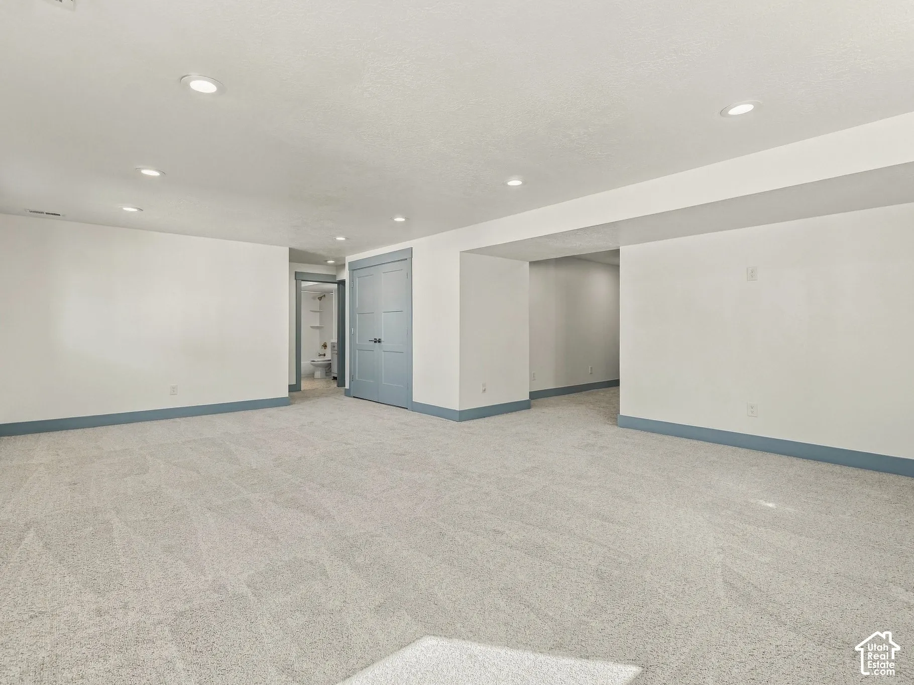 Expansive interior room featuring neutral carpeting, recessed lighting, and painted grey dual-panel closet doors