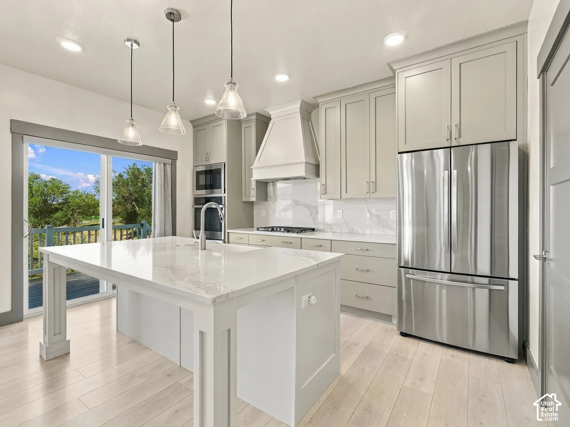 Kitchen featuring shaker-style cabinetry, an expansive central island with stone-finish countertops, stainless steel appliances, a custom range hood, and wood-finish flooring