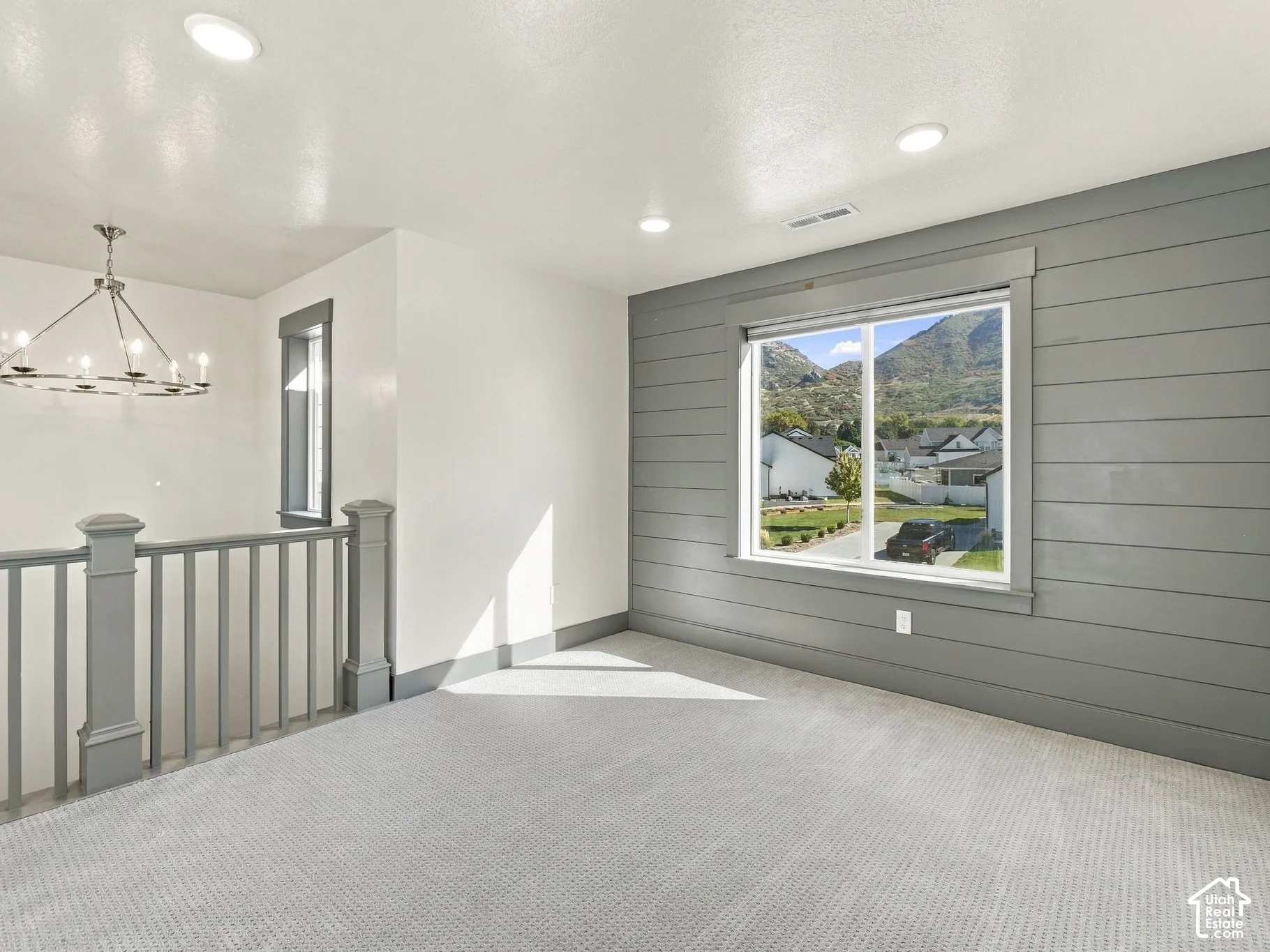 Room featuring a grey horizontal shiplap accent wall, neutral carpeting, recessed ceiling lighting, a modern multi-arm chandelier, and a painted wood balustrade
