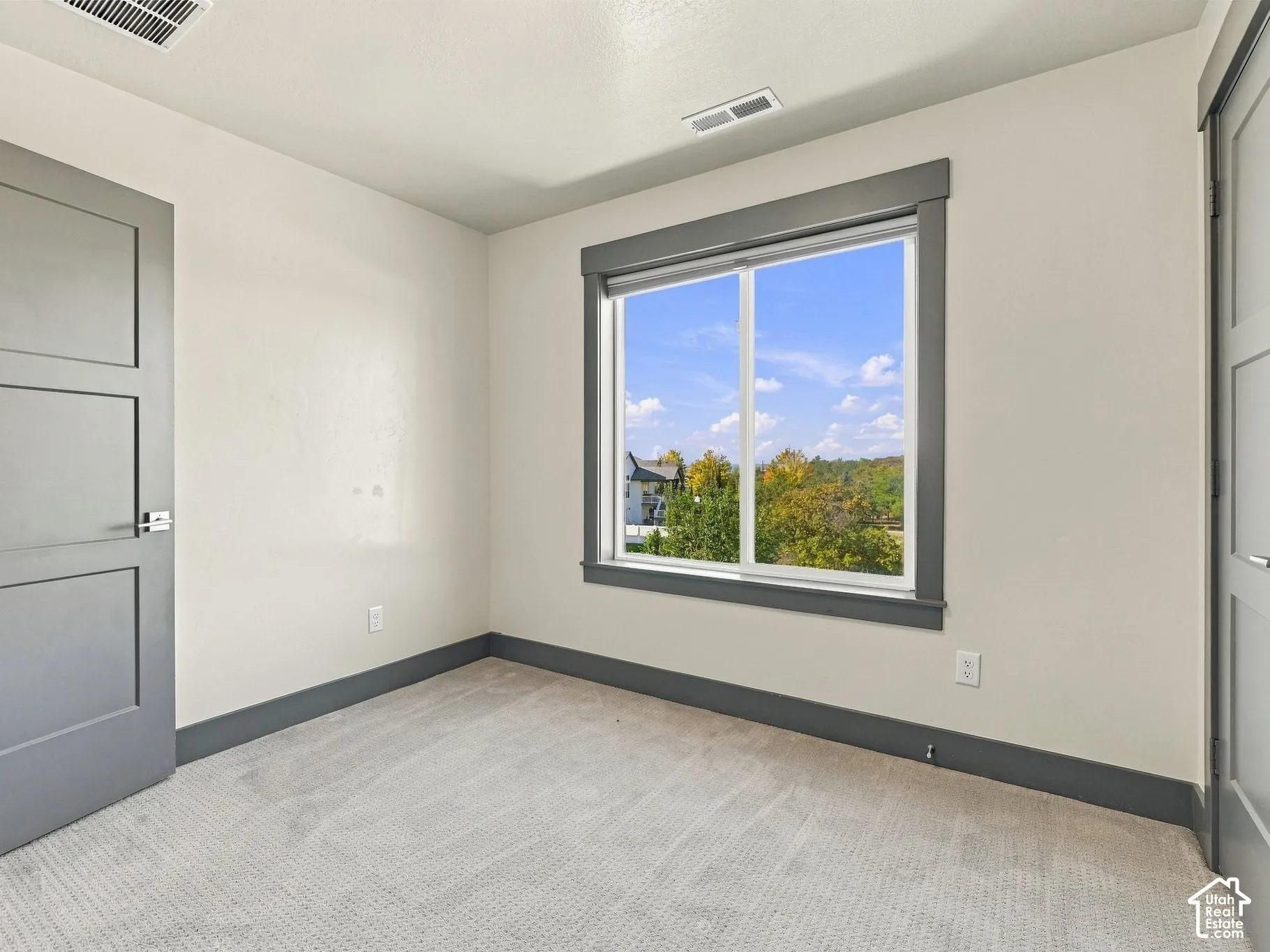 Interior space featuring light-toned carpeting, two-panel interior doors with metallic lever handles, and a window with gray trim casing