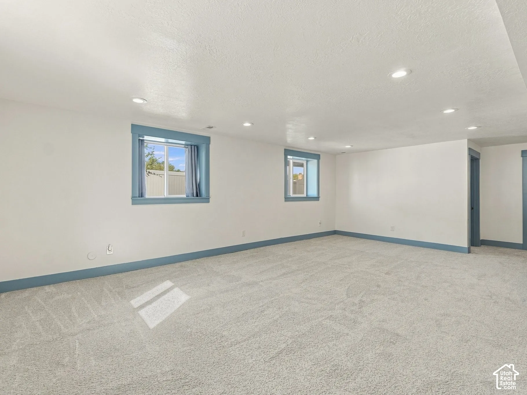 Expansive interior space featuring neutral wall-to-wall carpeting, recessed ceiling lighting, and dual windows with blue-toned trim