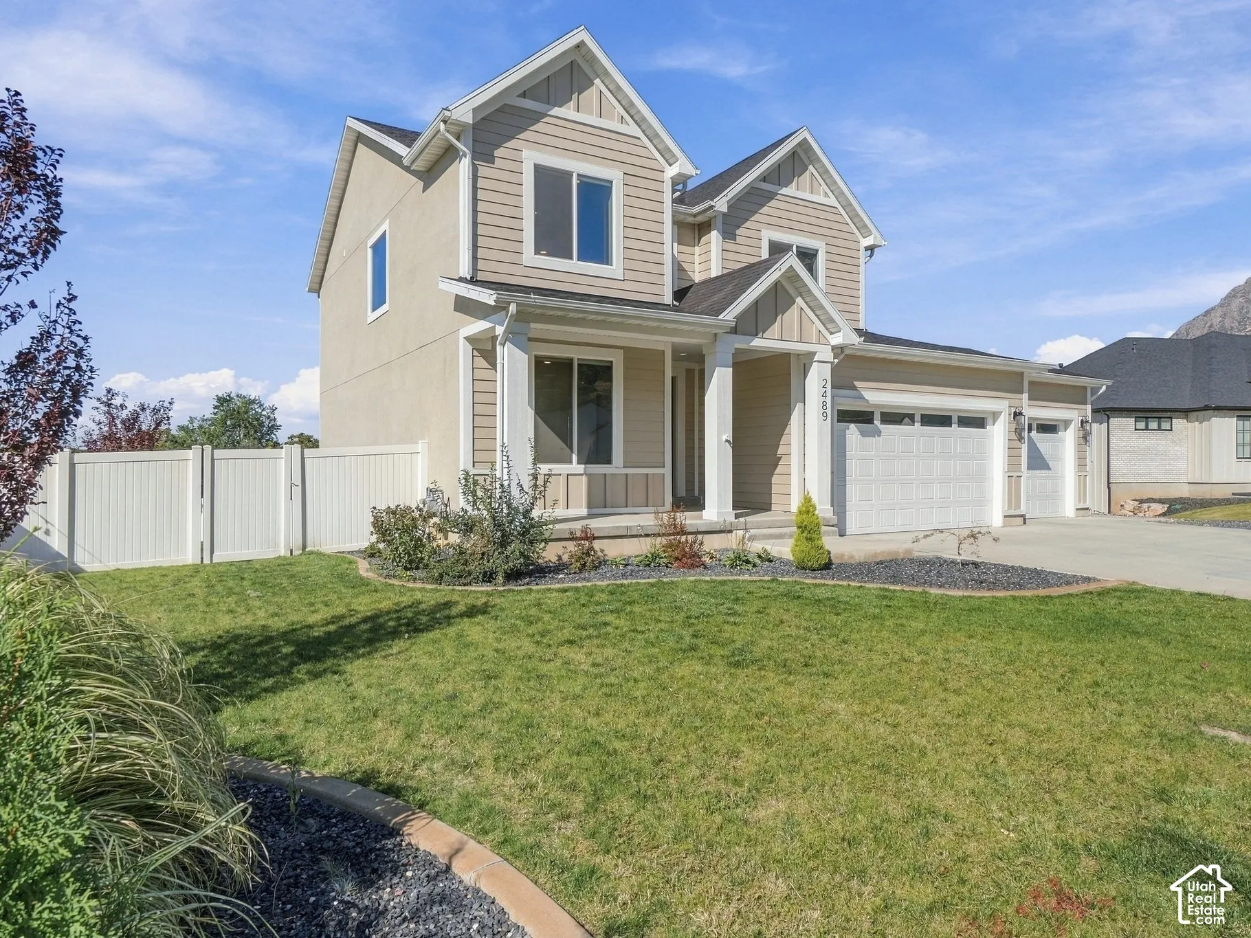 Two-story exterior featuring tan horizontal siding, stucco finish, a concrete driveway, a three-car garage, and a white privacy fence