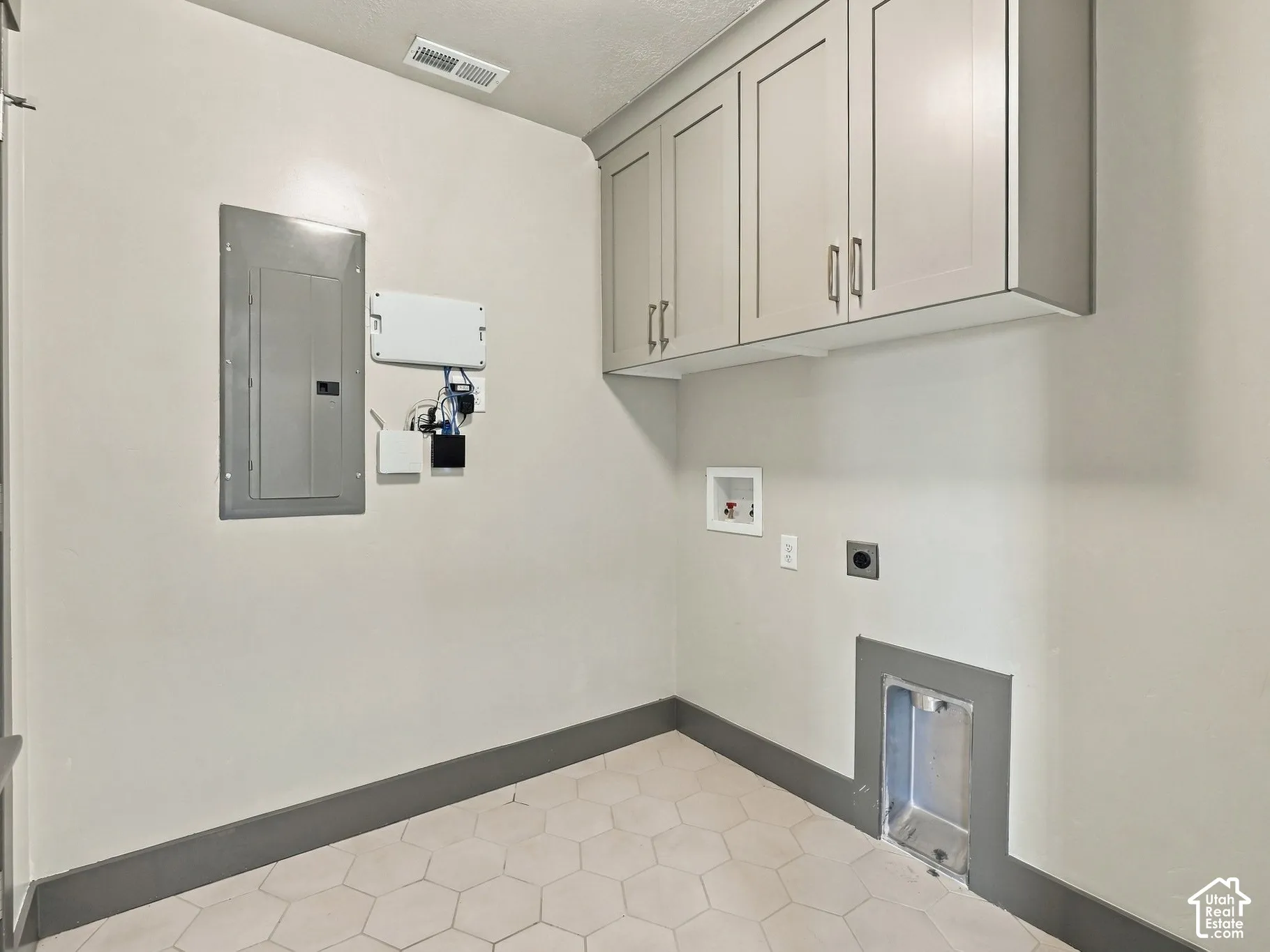 Utility space featuring wall-mounted shaker-style cabinetry, hexagon-patterned tile flooring, and integrated laundry hookups
