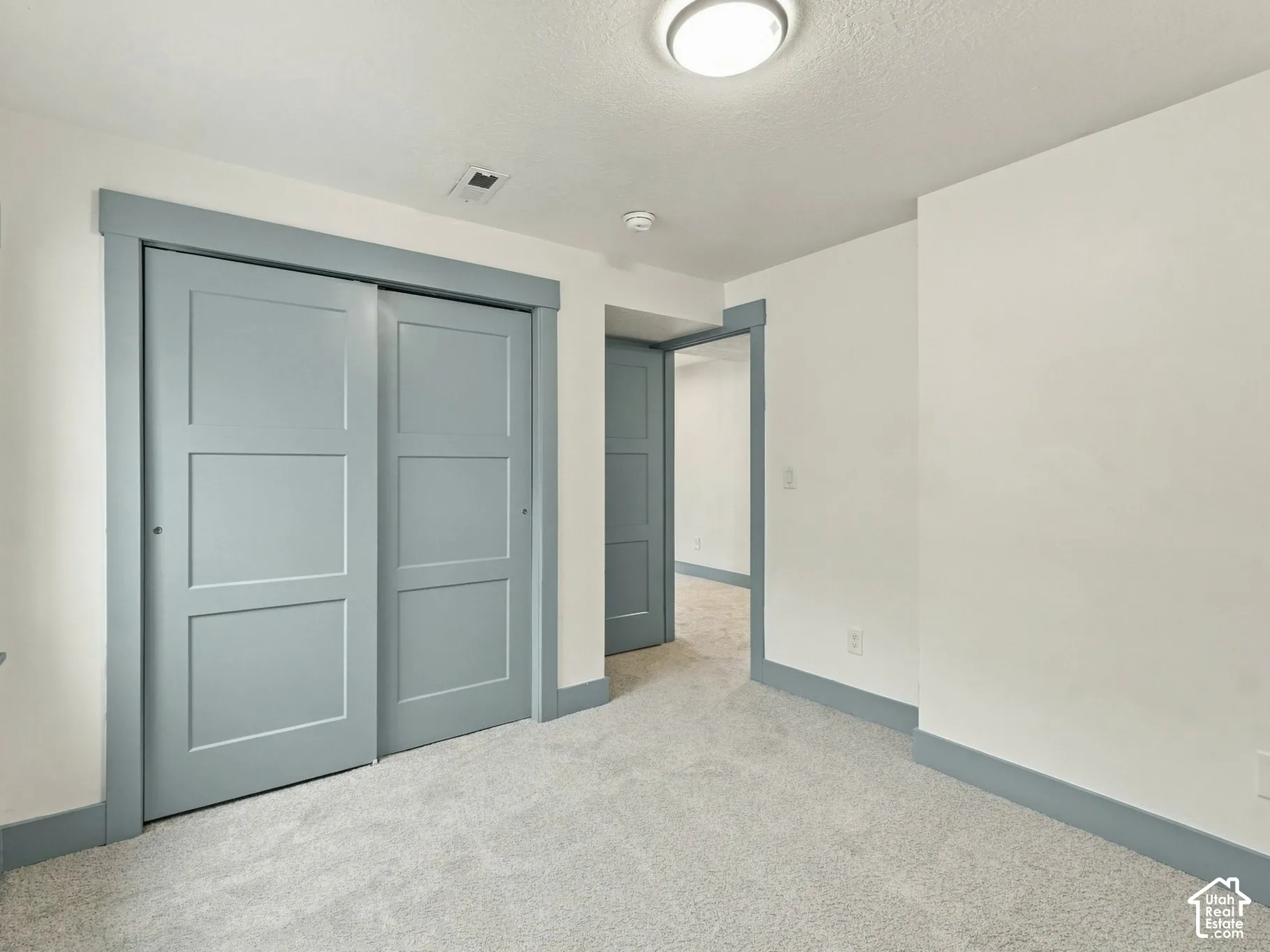 Neutral interior room featuring plush carpeting, dual-panel sliding closet doors, and contrasting painted wood trim