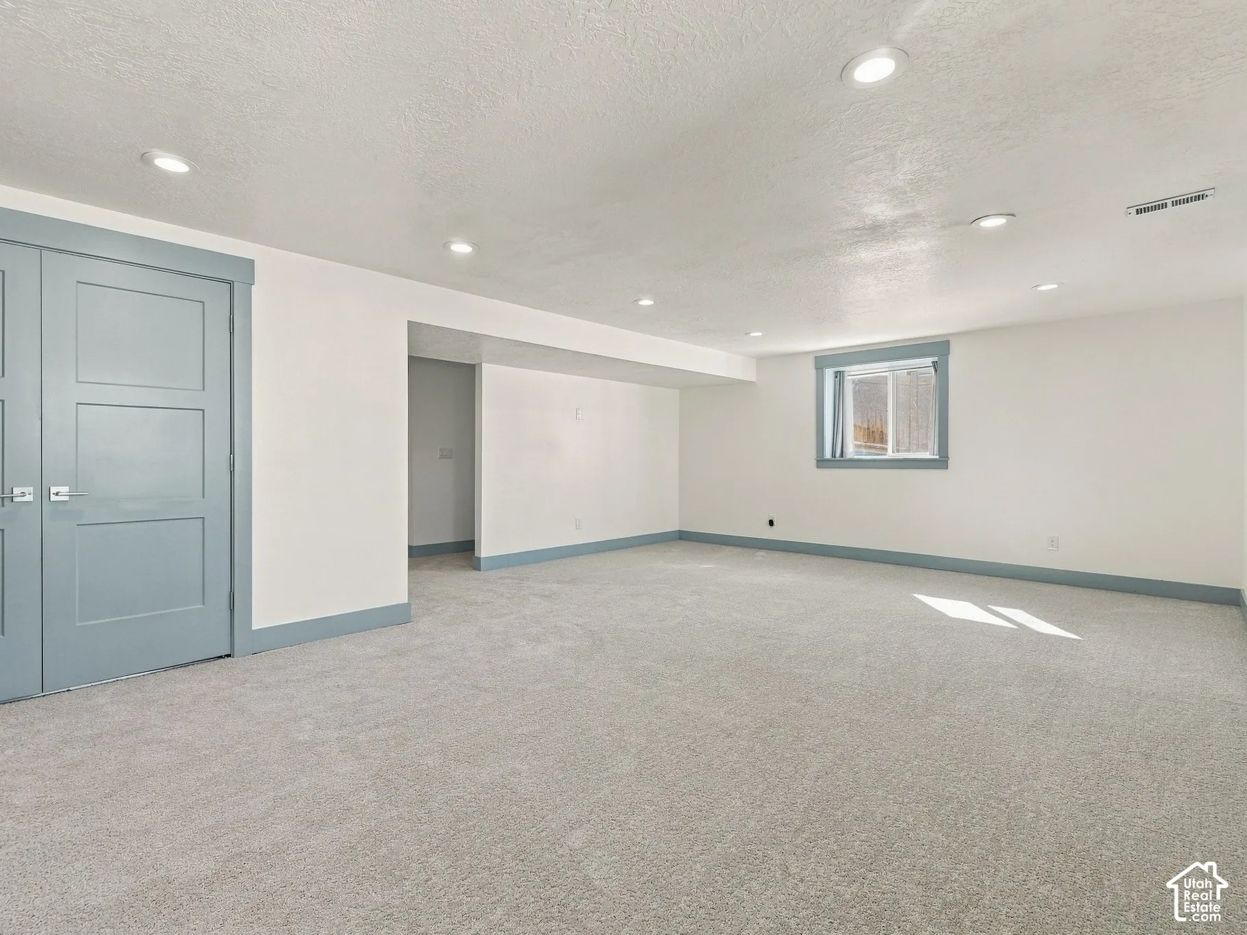 Interior space featuring neutral wall-to-wall carpeting, recessed ceiling lighting, double doors with blue trim, and a window with matching blue casing