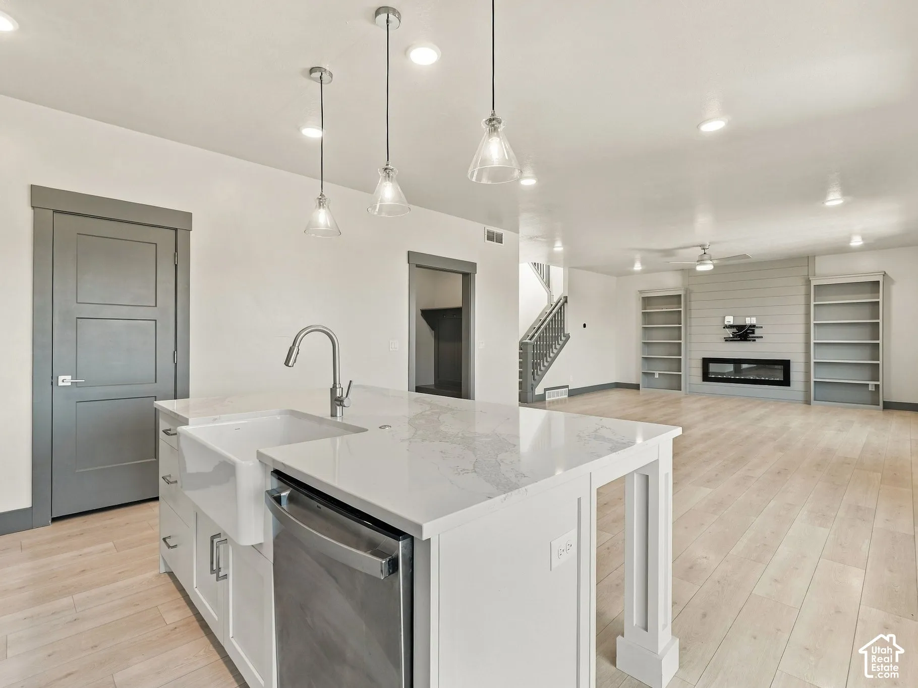 Kitchen island featuring a farmhouse sink, stone-surface countertop, and pendant lighting, complemented by wood-finish flooring, built-in shelving, and a horizontal-plank fireplace wall