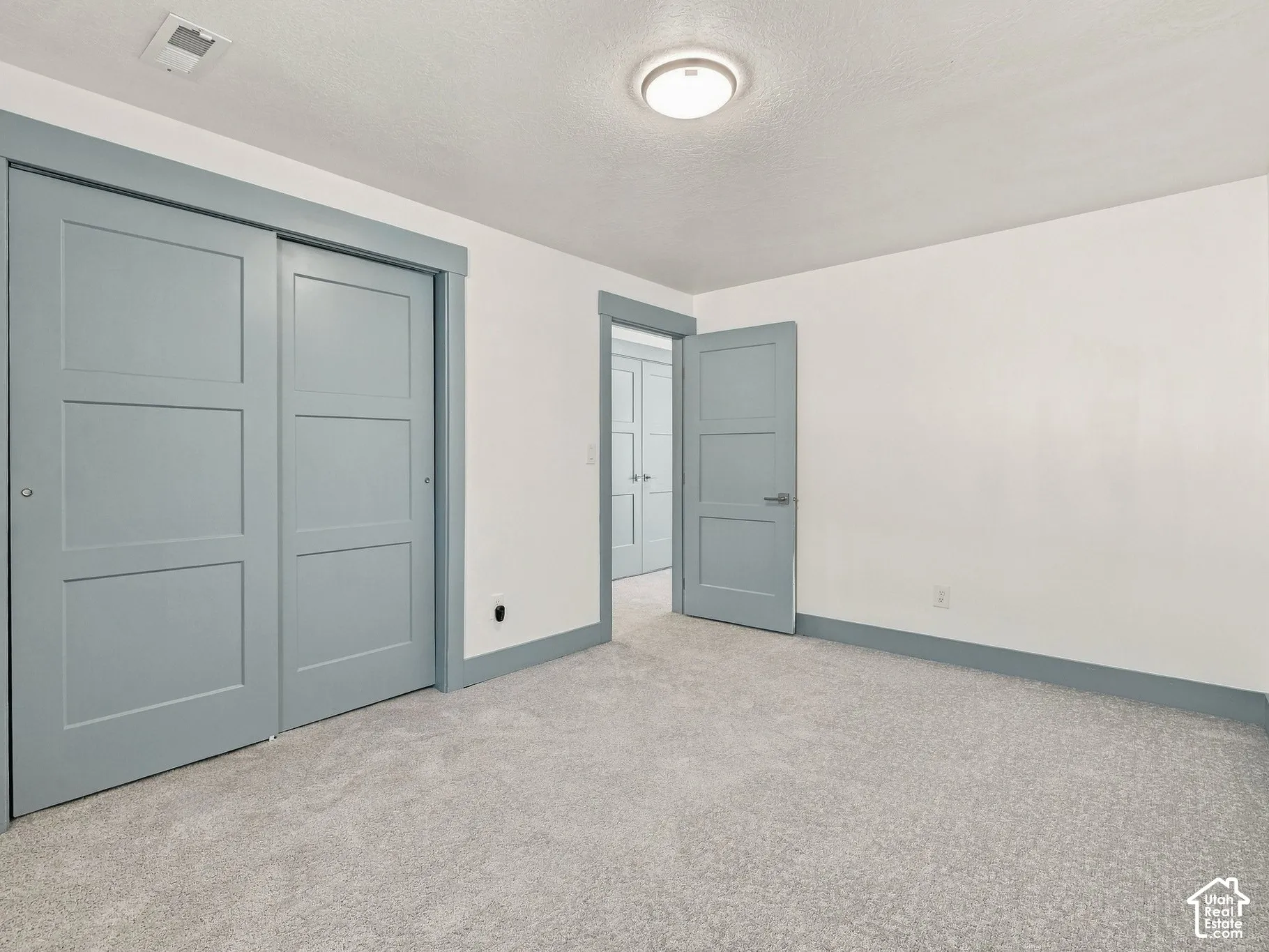 Neutral-toned interior space featuring light blue three-panel doors, matching blue door trim, neutral wall-to-wall carpeting, and a central flush-mount ceiling light fixture