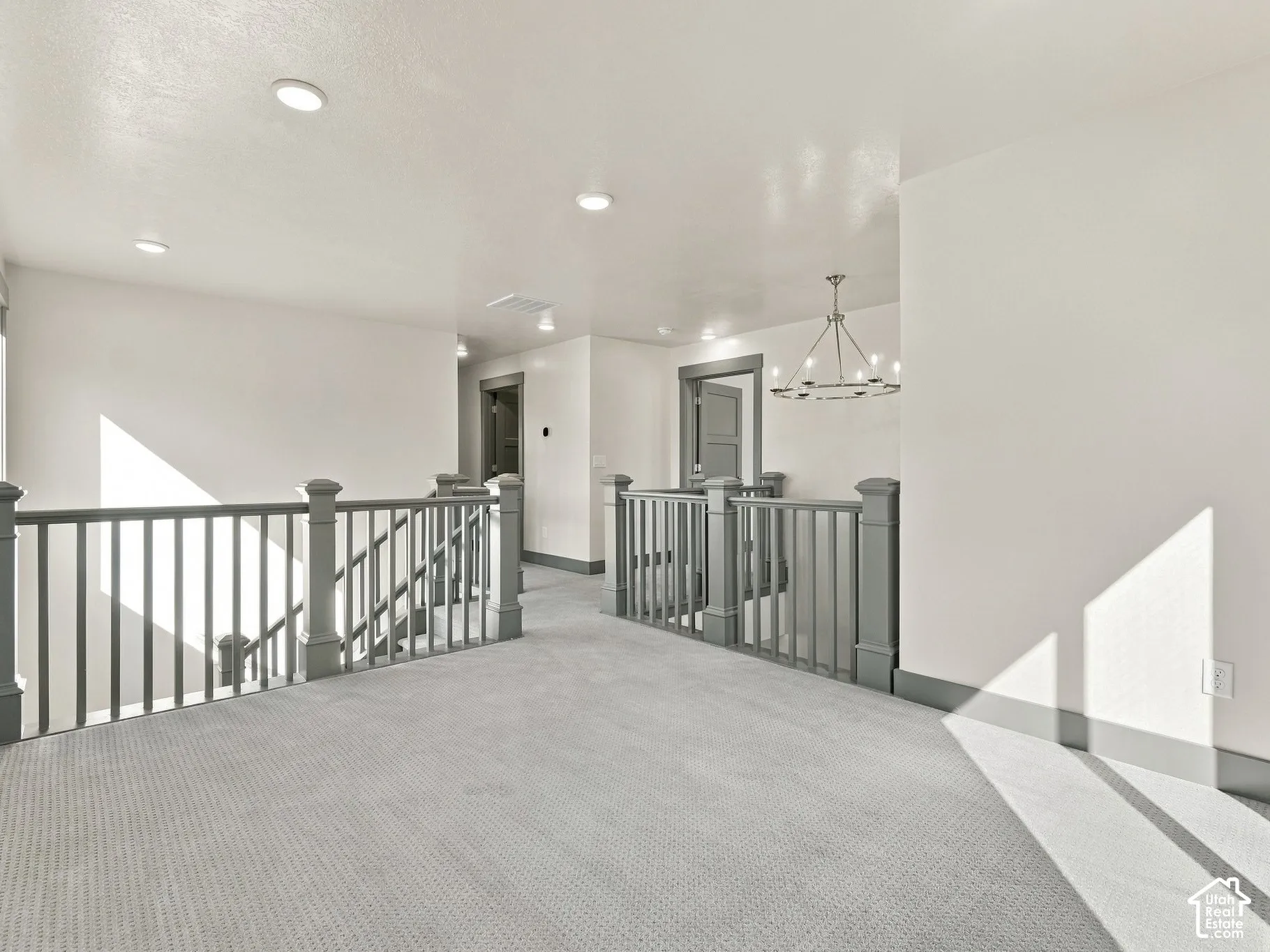 Open landing area featuring wall-to-wall carpeting, recessed ceiling lighting, a modern metal chandelier, and a painted wooden staircase railing