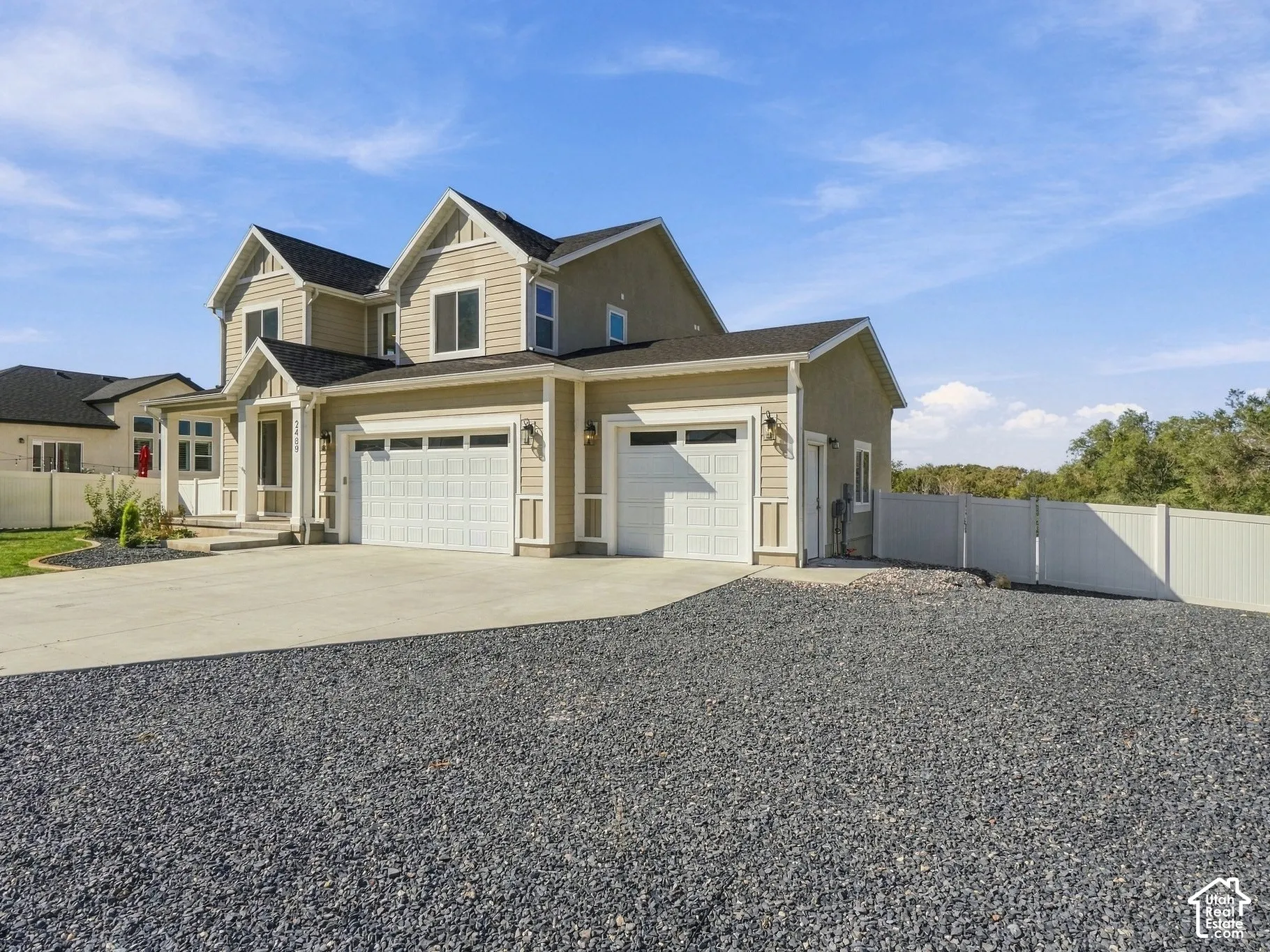 Two-story exterior featuring tan horizontal siding, a multi-gabled roofline, a concrete driveway, an attached three-car garage, and perimeter vinyl fencing