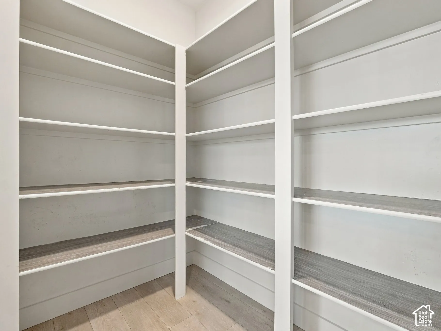 Walk-in pantry featuring white custom built-in shelving, wood-finish flooring, and multi-tier storage configurations