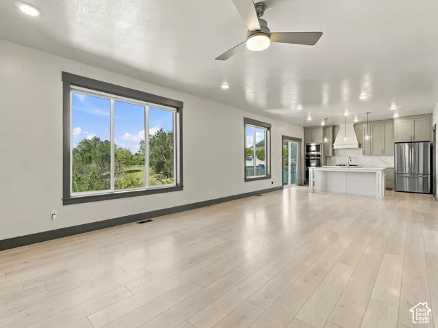 Open-concept interior featuring light wood-finish flooring, recessed lighting, a modern ceiling fan, large windows with dark trim, and a kitchen equipped with a central island and stainless-steel appliances