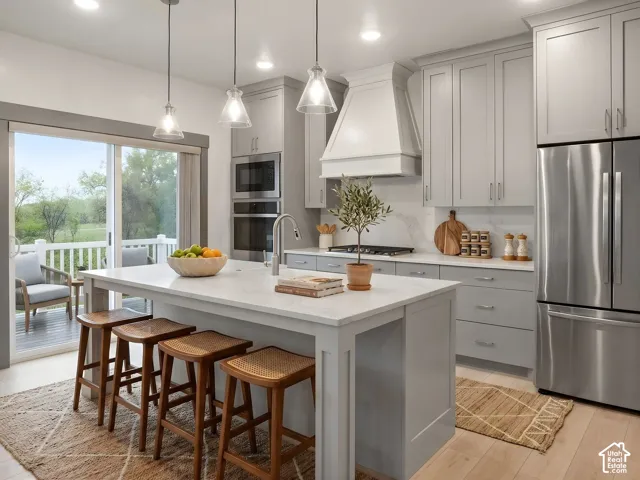 Kitchen featuring light-gray shaker-style cabinetry, quartz countertops, stainless steel appliances, a custom range hood, and wood-finish flooring