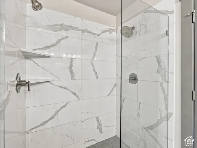 Walk-in shower featuring large-format porcelain tile with veining, glass panel enclosure, dual shower heads, and integrated corner shelving