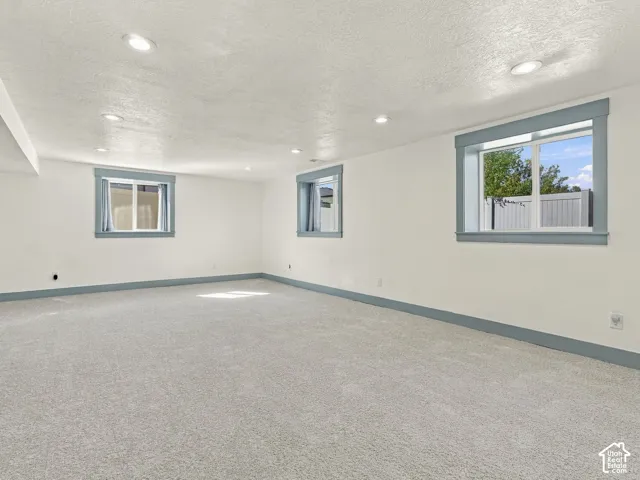 Neutral-toned wall-to-wall carpeting, recessed ceiling lighting, and windows featuring blue-toned trim