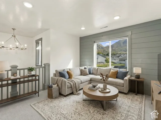 Living area featuring a horizontal plank accent wall, large picture window, modern wheel-style chandelier, and neutral wall-to-wall carpeting