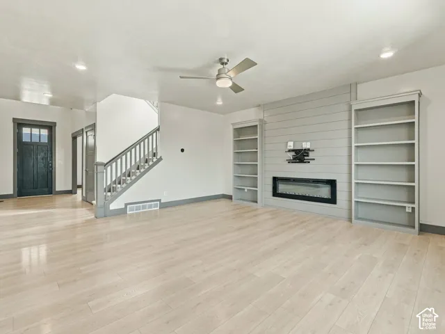 Light-toned wood-finish flooring, shiplap fireplace surround with an integrated electric linear fireplace, and custom built-in shelving