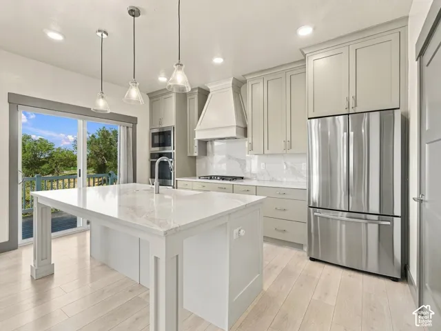 Kitchen featuring shaker-style cabinetry, an expansive central island with stone-finish countertops, stainless steel appliances, a custom range hood, and wood-finish flooring