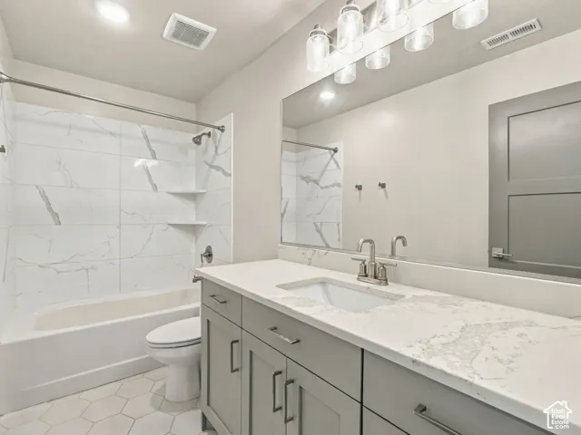 Bathroom featuring a stone-patterned countertop, shaker-style vanity cabinetry, hexagon floor tile, tub-shower combination with floor-to-ceiling tile surround, and an expansive wall-to-wall mirror
