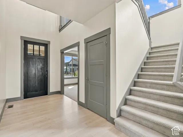 Entryway featuring a high-contrast palette, wood-finish flooring, a multi-pane glass panel door, grey door casings, and a carpeted staircase with a white handrail