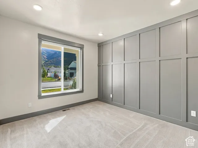 Accent wall featuring extensive board and batten detailing, neutral wall-to-wall carpeting, recessed ceiling lighting, and window casing framing a mountain backdrop
