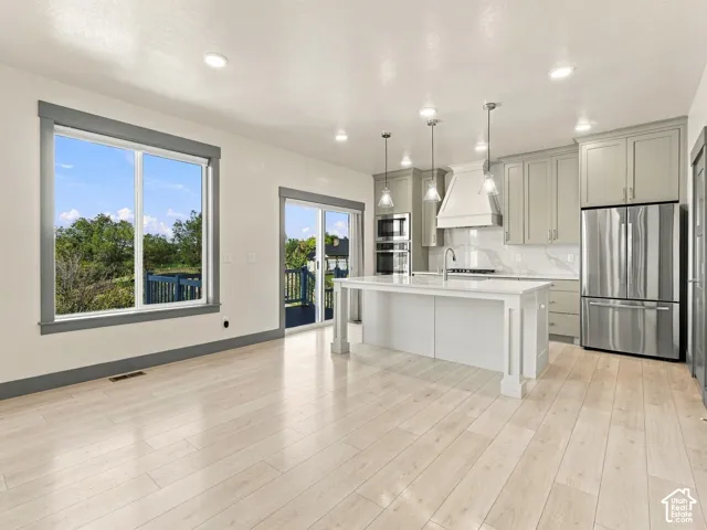 Kitchen featuring a central island with a quartz countertop, custom cabinetry, stainless steel appliances, wood-finish flooring, and pendant lighting