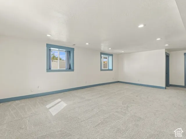 Expansive interior space featuring neutral wall-to-wall carpeting, recessed ceiling lighting, and dual windows with blue-toned trim