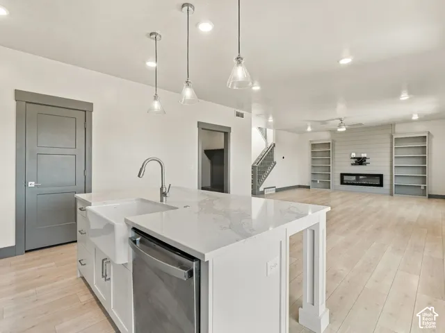 Kitchen island featuring a farmhouse sink, stone-surface countertop, and pendant lighting, complemented by wood-finish flooring, built-in shelving, and a horizontal-plank fireplace wall