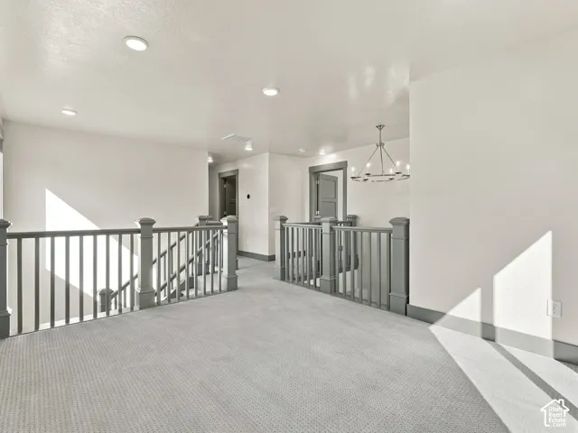 Open landing area featuring wall-to-wall carpeting, recessed ceiling lighting, a modern metal chandelier, and a painted wooden staircase railing