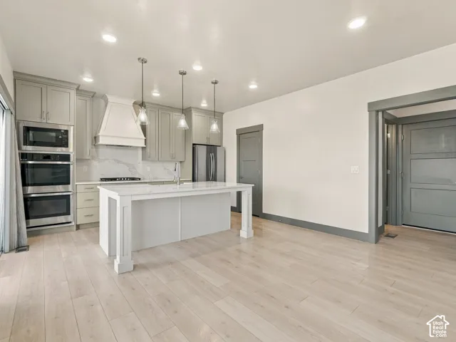 Kitchen featuring light-toned wood-finish flooring, a central island with a quartz countertop, custom cabinetry, stainless steel double wall ovens, and pendant lighting