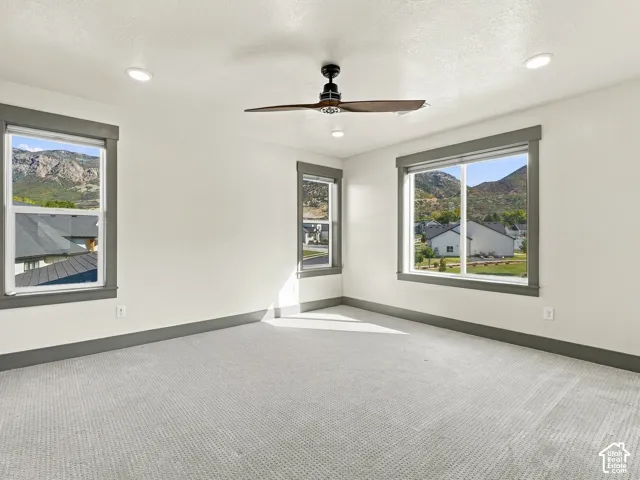 Room featuring neutral carpeting, recessed lighting, a ceiling fan with dark wood-finish blades, and dark-trimmed windows framing mountain scenery